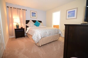 A bedroom with a bed, a nightstand, a lamp, a dresser, and two framed pictures on the wall.