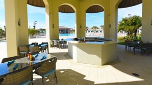An outdoor patio area with tables and chairs, a pool, and a bar. - Champions Gate IHR 3012 (Davenport)