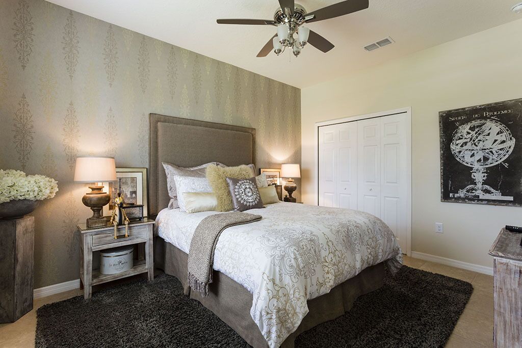 A bedroom with a large bed, two bedside tables with lamps, a ceiling fan, and a door.