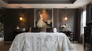 Quarto com cama grande, paredes escuras e um quadro sobre a cama.