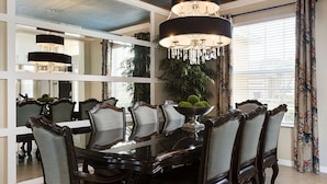 Uma área de jantar com uma mesa redonda grande, cadeiras ricamente decoradas e um candelabro.
