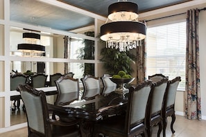Enjoy meals in this elegant dining area with a large table and comfortable seating for six, illuminated by stylish chandeliers and a large mirror.
