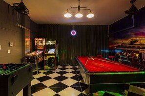 Une salle de billard équipée d’une table de billard, d’un baby-foot et de jeux d’arcade.