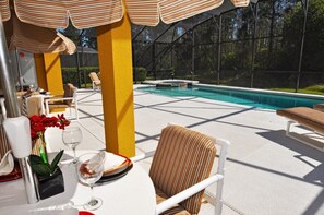 An outdoor pool area with lounge chairs, a table set for dining, and a covered seating area.