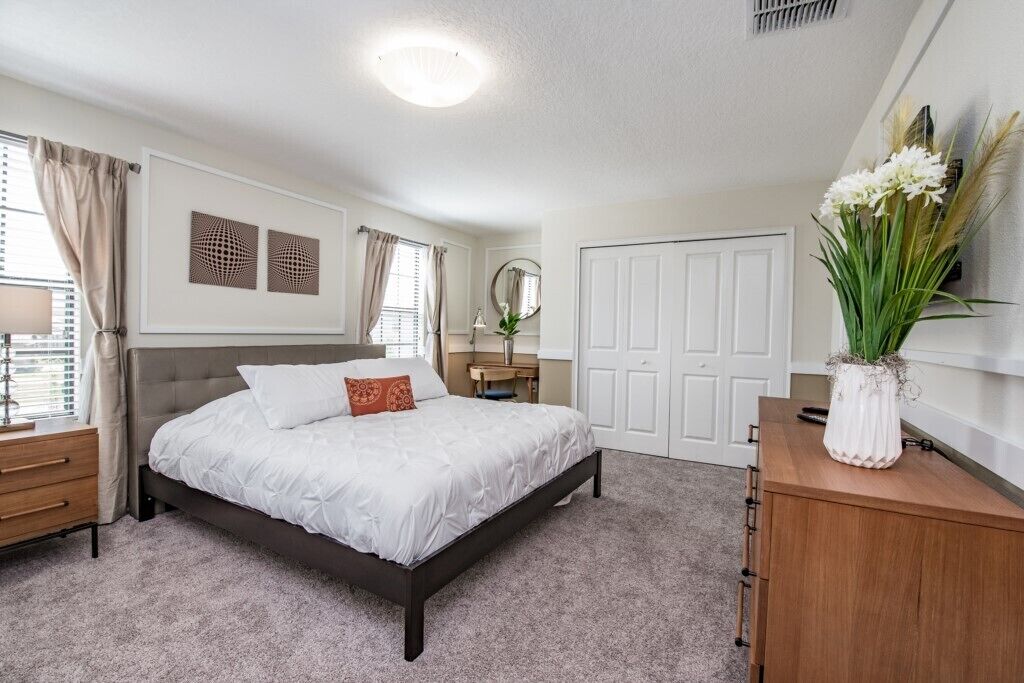 A bedroom with a bed, a dresser, a mirror, and a vase with flowers.