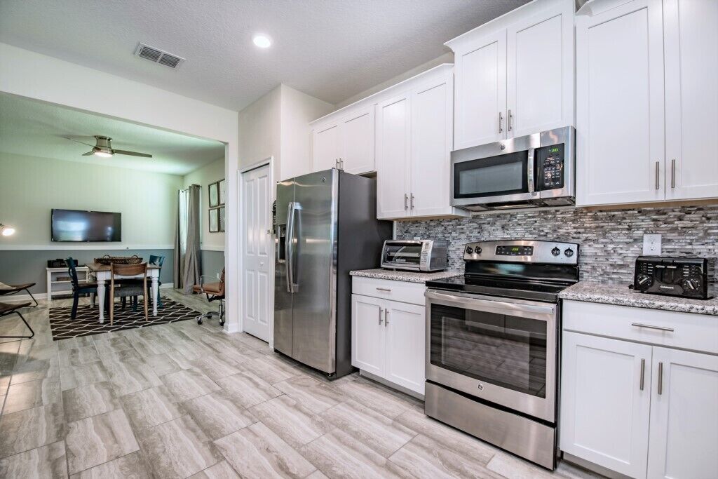 A modern kitchen with white cabinets, stainless steel appliances, and a stone backsplash.