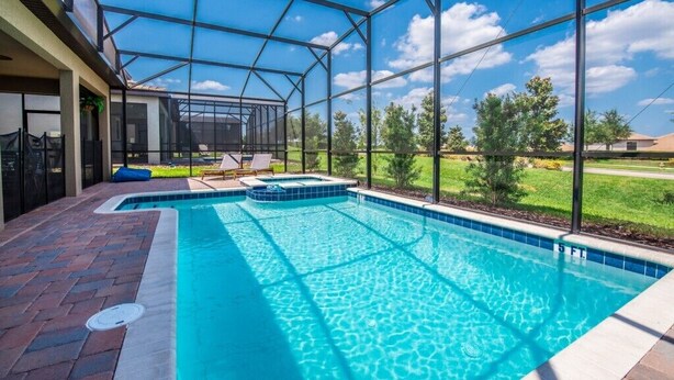 A swimming pool with a glass enclosure, surrounded by a brick patio and a view of a green landscape. - Champions Gate IHR 4029 (Davenport)