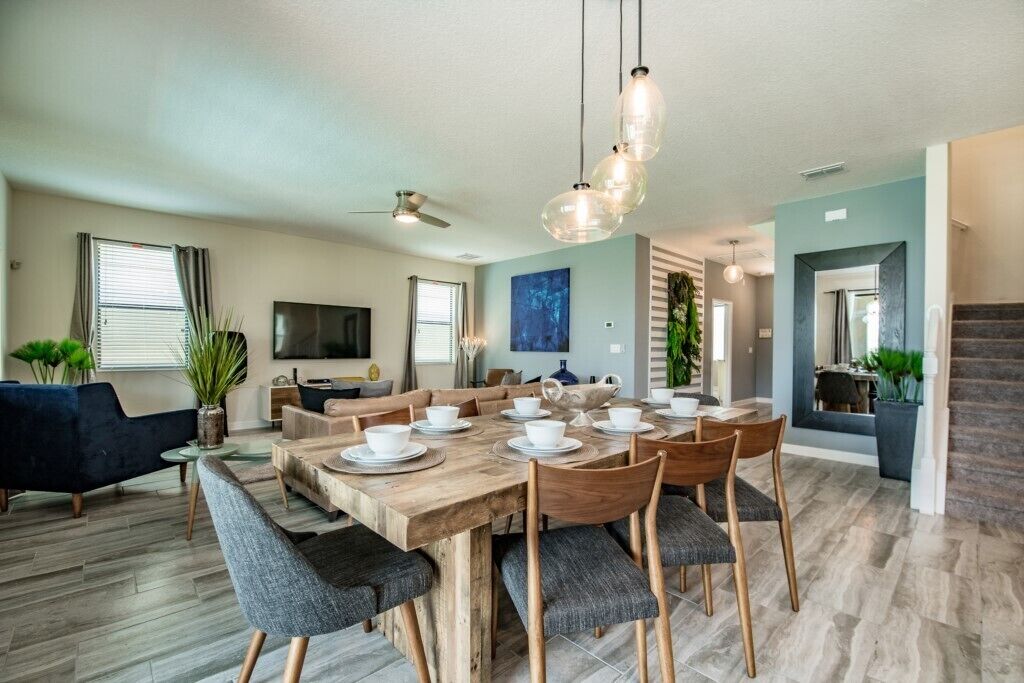 Ein modernes Wohnzimmer mit einem Holzesstisch, gedeckt für vier Personen, einer Couch, einem Fernseher und einer Treppe, die zu einer anderen Ebene führt.