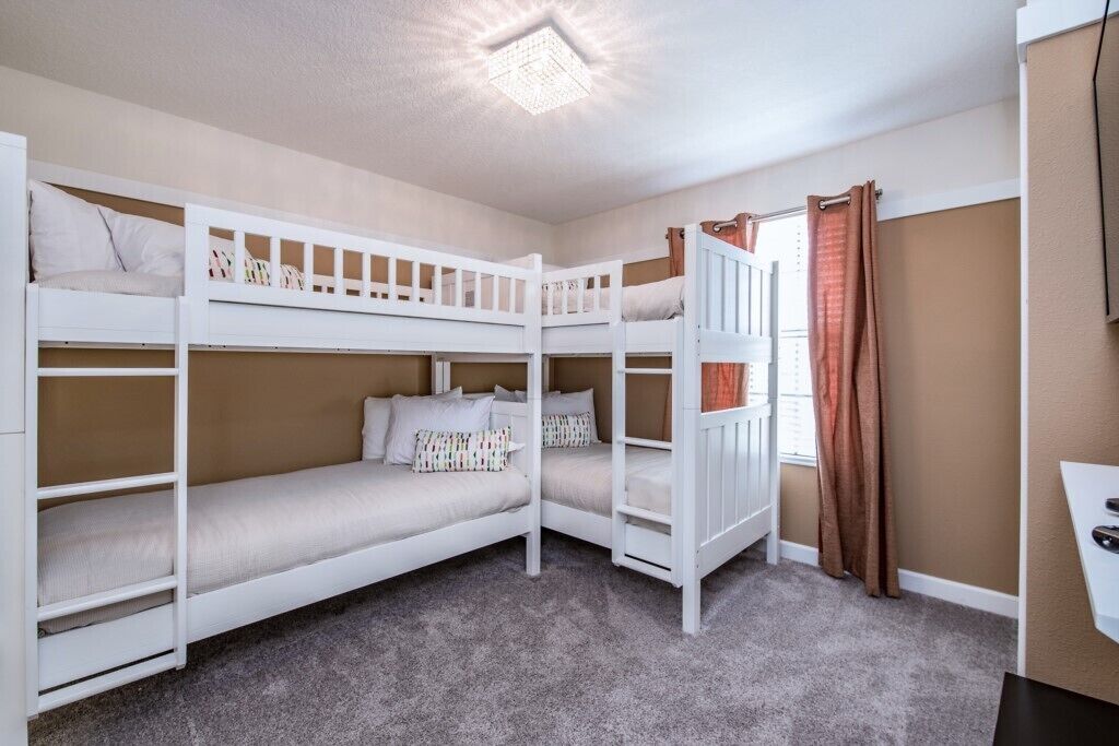 A bunk bed room with a desk and a window with curtains.