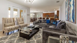 Ein modernes Wohnzimmer mit einem Ecksofa, zwei Sesseln, einem Couchtisch und einem Essbereich im Hintergrund.