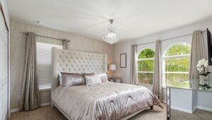Ein Schlafzimmer mit einem gebürsteten Kopfstück, einem großen Bett, einer Kristallleuchtre und Blick auf Grün durch die Fenster.