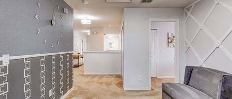 Un interior moderno con una pared gris con diseño, un sofá gris y un pasillo que conduce a una habitación con una puerta blanca.