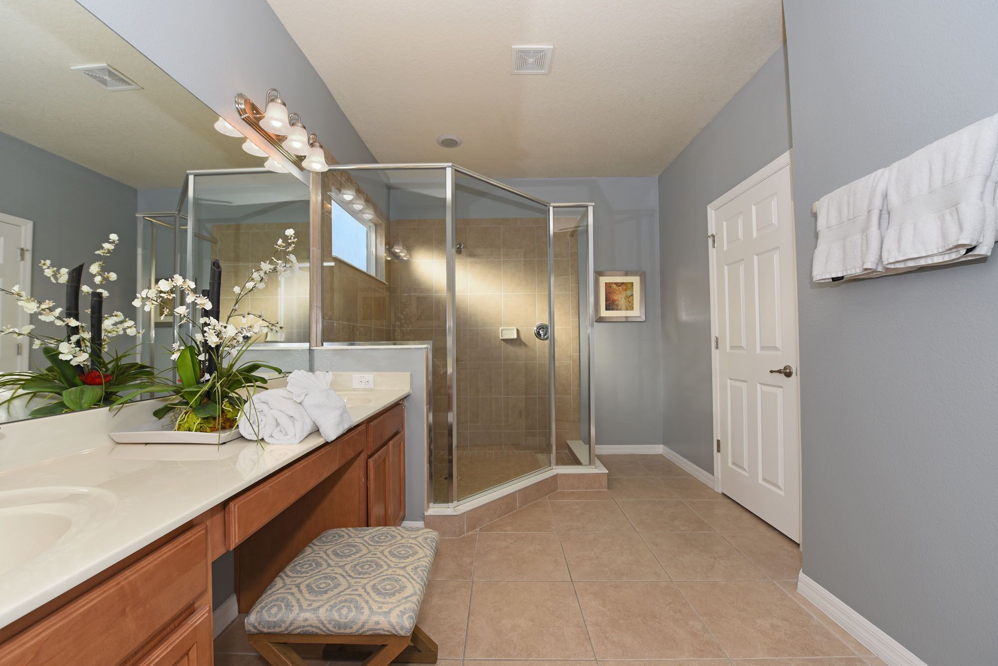 A modern bathroom with a glass shower enclosure, a vanity with a mirror, and a bench.