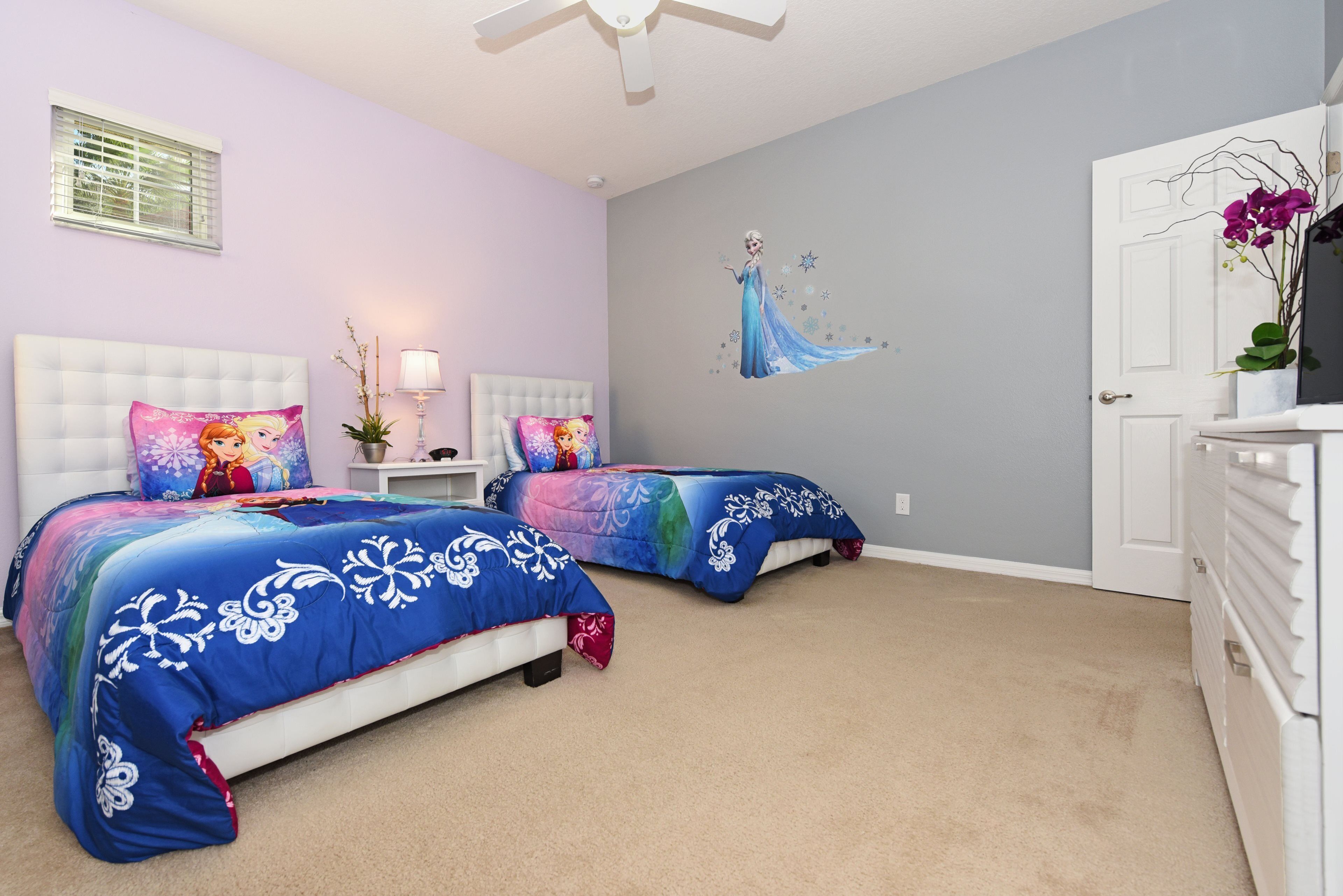 A bedroom with two beds, a ceiling fan, a wall mural, and a door with a plant.