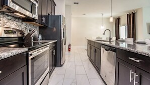 A modern kitchen with dark cabinetry, stainless steel appliances, and a tiled backsplash. - 4 Bedroom 3 Bathroom Townhome w Pool (Davenport)