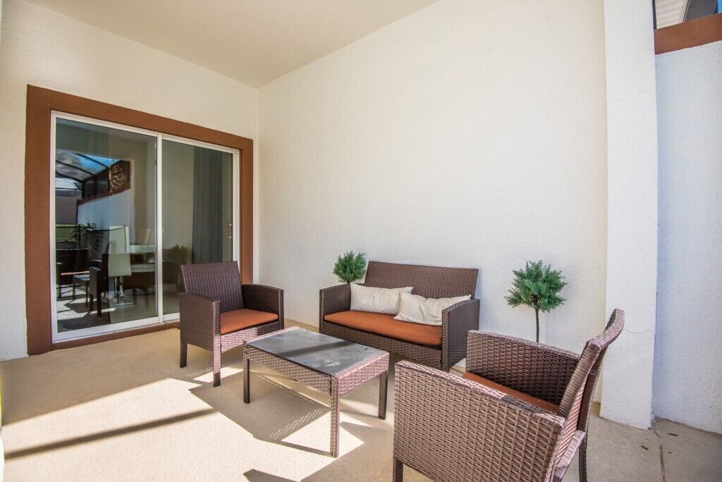A sunlit outdoor seating area with wicker furniture, a glass door leading to a balcony, and a small potted plant.