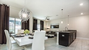 A modern kitchen with a central island, a dining area with white chairs, and a large chandelier. - 4 Bedroom 3 Bathroom Townhome w Pool (Davenport)