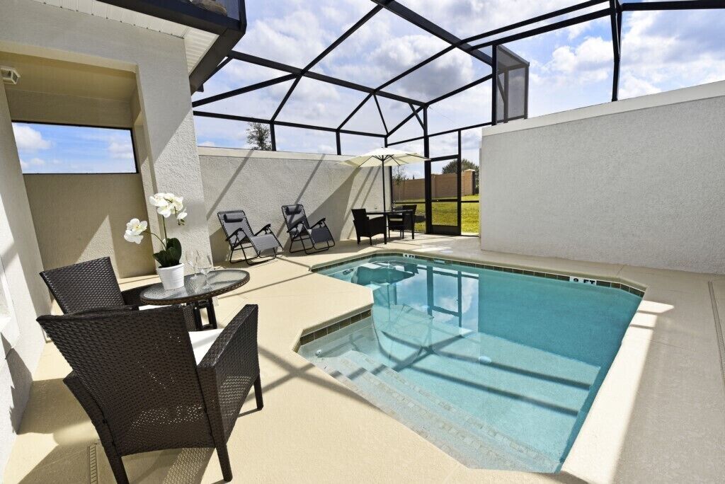 An outdoor swimming pool with lounge chairs and a table, surrounded by a covered patio area.