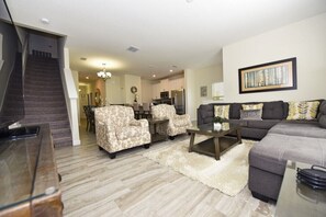 A living room with a sofa, armchairs, a coffee table, and a staircase leading to a kitchen. - Champions Gate IHR 3014 (Davenport)