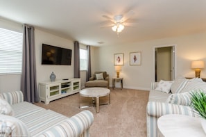 A living room with a sofa set, a coffee table, a TV on the wall, and a ceiling fan. - Champions Gate IHR 4035 (Davenport)