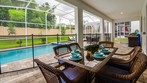 Un patio cubierto con piscina, mobiliario de mimbre y una mesa lista para comer.