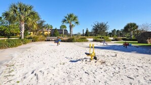 A sandy beach area with playground equipment and palm trees.