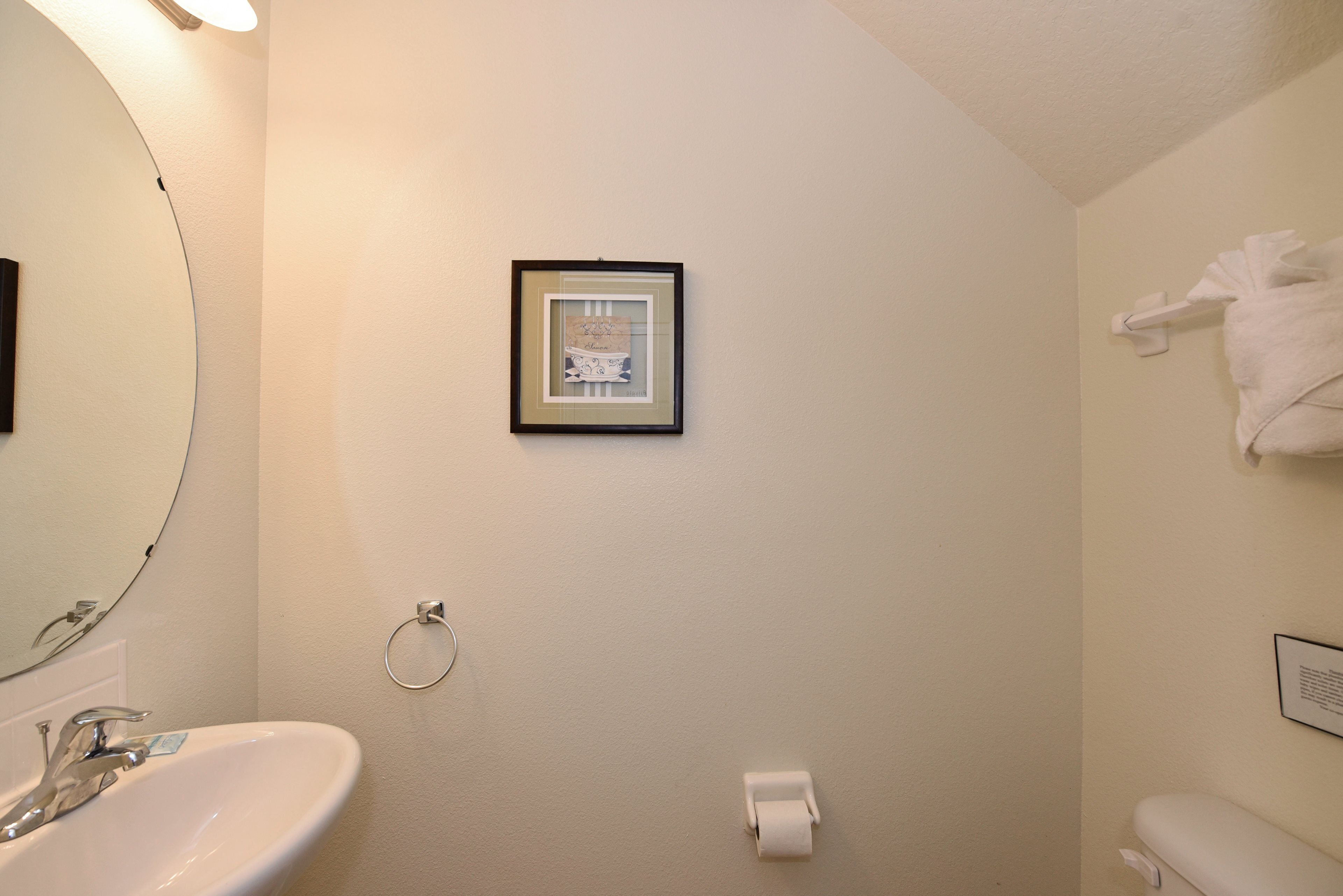 A bathroom with a sink, mirror, framed picture, towel rack, and toilet.