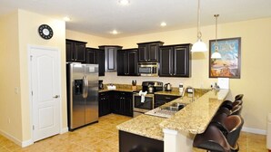 Una cocina moderna con armarios oscuros, electrodomésticos de acero inoxidable, encimera de granito y una zona de bar con taburetes.