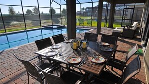 Un patio exterior con piscina, mesa de comedor lista con platos y vasos, y mobiliario de jardín.