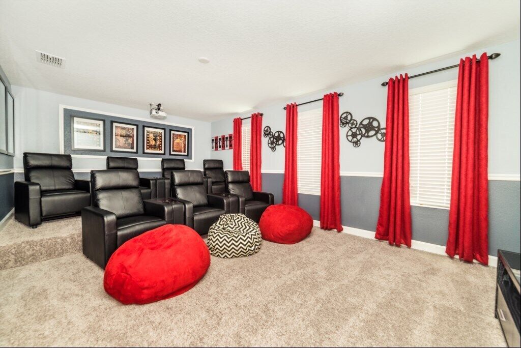 A home theater room with black leather recliners, red curtains, and a carpeted floor.