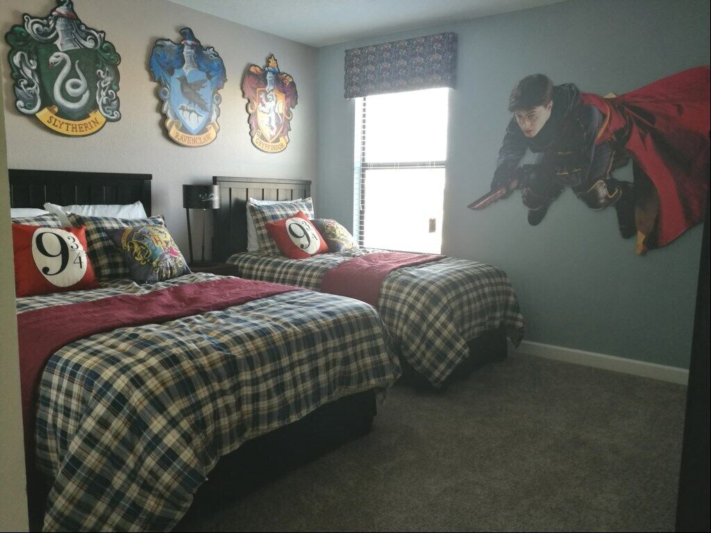 A bedroom with two beds, a window, and three Hogwarts house crest wall decorations.