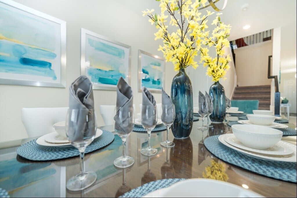 A dining table set with plates, bowls, and wine glasses, accompanied by a vase of yellow flowers.