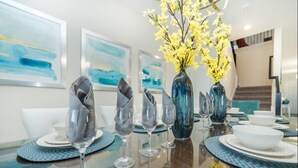 Une table à manger dressée avec des assiettes, des bols et des verres à vin, agrémentée d’un vase rempli de fleurs jaunes.