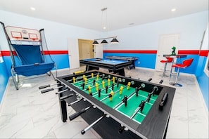 A room with a foosball table, a basketball hoop, and a pool table.