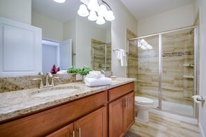 A modern bathroom with a granite countertop, a double sink, wooden cabinets, a glass shower enclosure, and a white toilet.