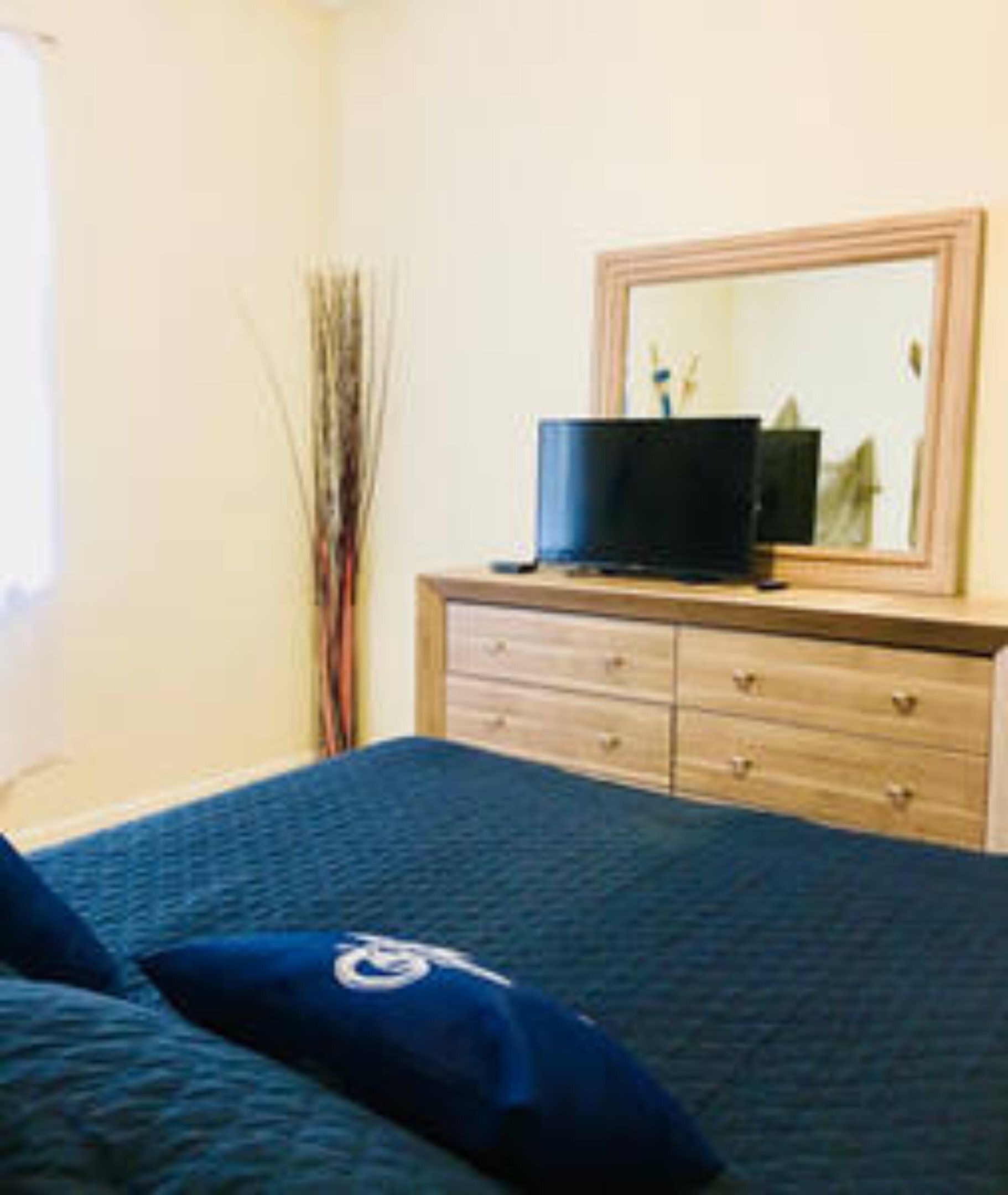 A bedroom with a bed, a dresser, a mirror, and a television on the dresser.