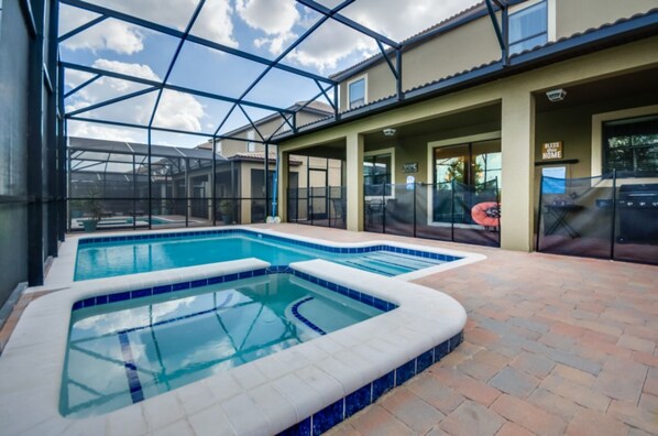 A swimming pool with a glass enclosure, a patio area, and a covered seating area.