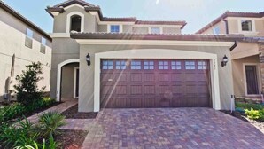 A two-story house with a large garage door, a covered driveway, and a small bell tower. - Luxury 5 Bedroom Private Pool IHR 1019 (Kissimmee)