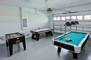 Sala de lazer com mesa de futebol de mesa, mesa de sinuca e um projetor.