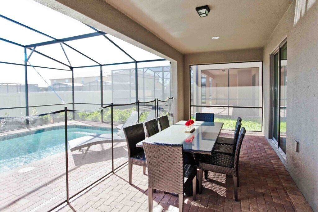 A covered patio area with a pool, a table with chairs, and a view of the surrounding area.