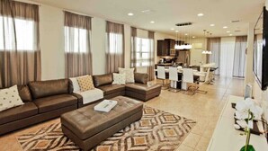 A modern living room with a sectional sofa, a dining area, and a kitchen in the background. - Luxury 5 Bedroom Private Pool IHR 1019 (Kissimmee)