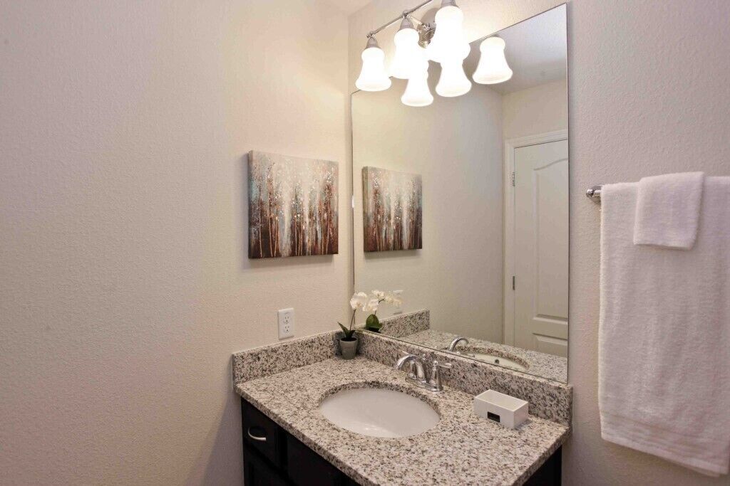 A bathroom with a granite countertop sink, a mirror, and two wall-mounted light fixtures.