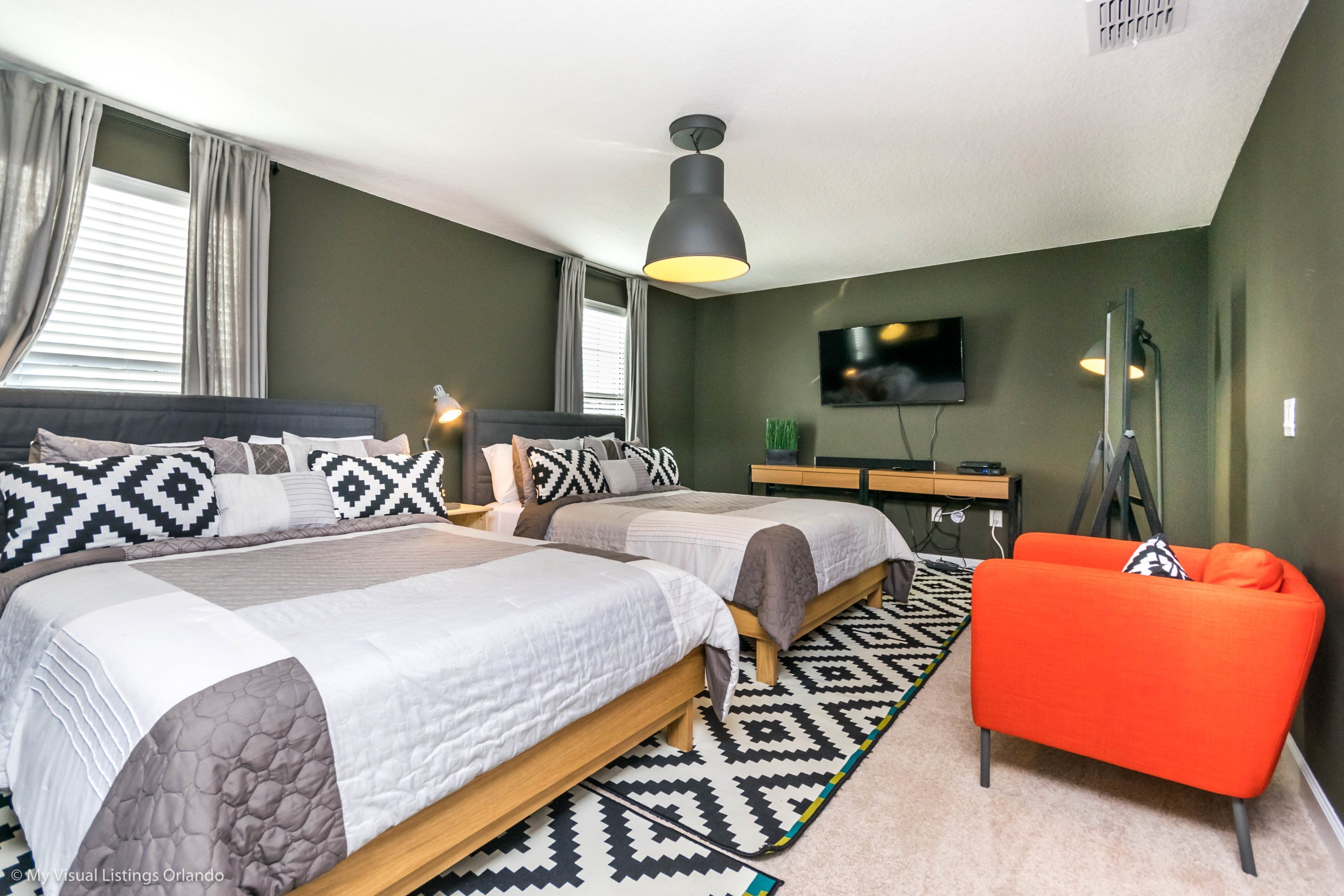 Une chambre avec deux lits, une télévision, un bureau et un fauteuil orange vif.