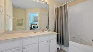 A bathroom with a vanity, mirror, lights, and a bathtub.