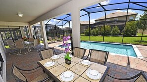 An outdoor patio with a pool, dining table set for six, and chairs.