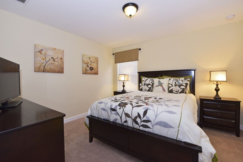 A bedroom with a bed, two bedside tables, a TV stand, and wall art.