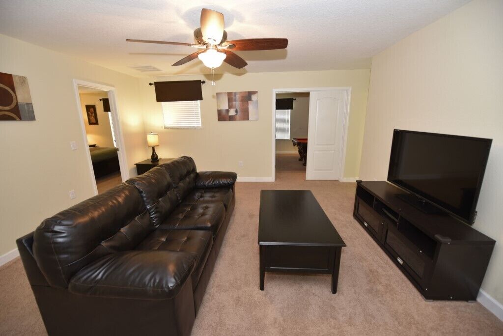 A living room with a leather sofa, a coffee table, a TV stand, and a ceiling fan.