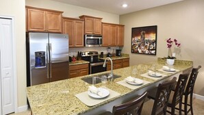 A modern kitchen with granite countertops, stainless steel appliances, wooden cabinets, and a cityscape artwork on the wall.