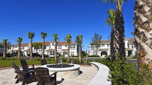 A patio with outdoor seating and a fire pit, surrounded by palm trees and a building with a tiled roof.