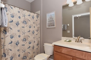 A bathroom with a shower curtain featuring a sea life pattern, a toilet, a sink with a mirror, and a framed picture on the wall.